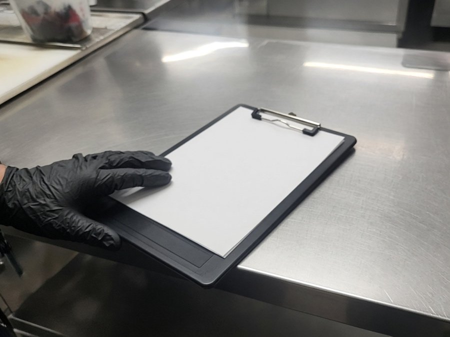 Clipboard and service tag on a stainless prep table — grease trap cleaning in Fullerton, CA